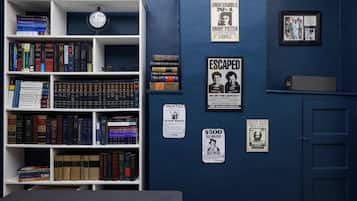A room with a bookshelf filled with books, a clock, and various posters on the wall.