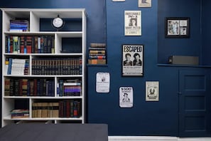 A room with a bookshelf filled with books, a clock, and various posters on the wall. - Jailhouse Rock Retreat {Arcade+Secret Passage} (Elizabethton)