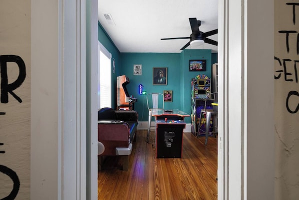A room with teal walls, a ceiling fan, a gaming console, and a couch.