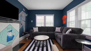 A living room with a sectional sofa, a coffee table, a striped rug, and a fireplace with a mural.