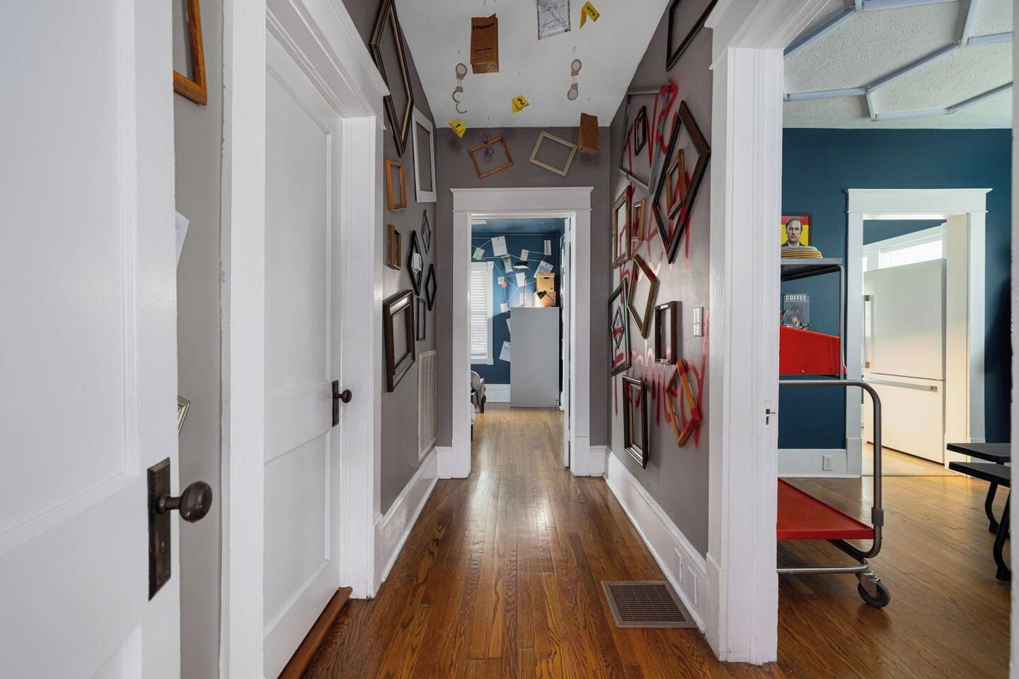 A hallway with wooden flooring, white walls, and a red cart.