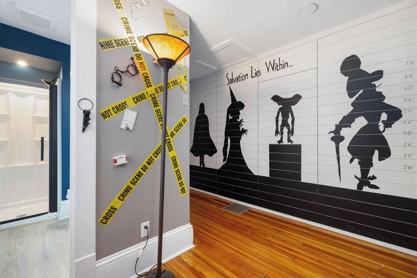 A room with a wall mural depicting silhouettes of characters, a lamp, and tape with 'CRIME SCENE DO NOT CROSS' text.