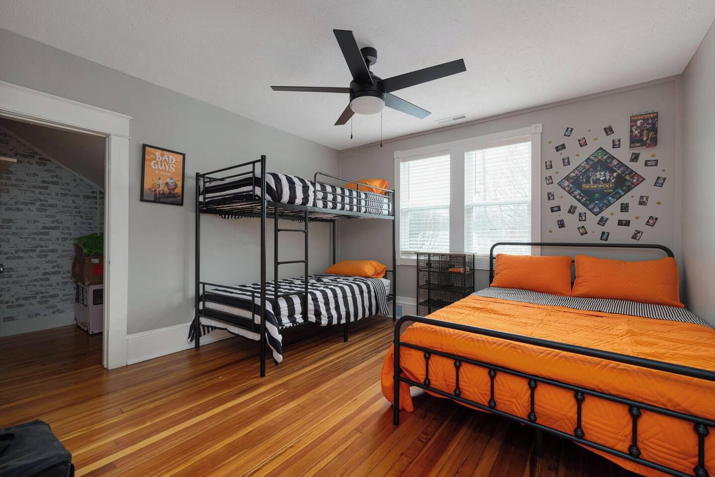A room with a bunk bed, a single bed, a ceiling fan, and a window with blinds.