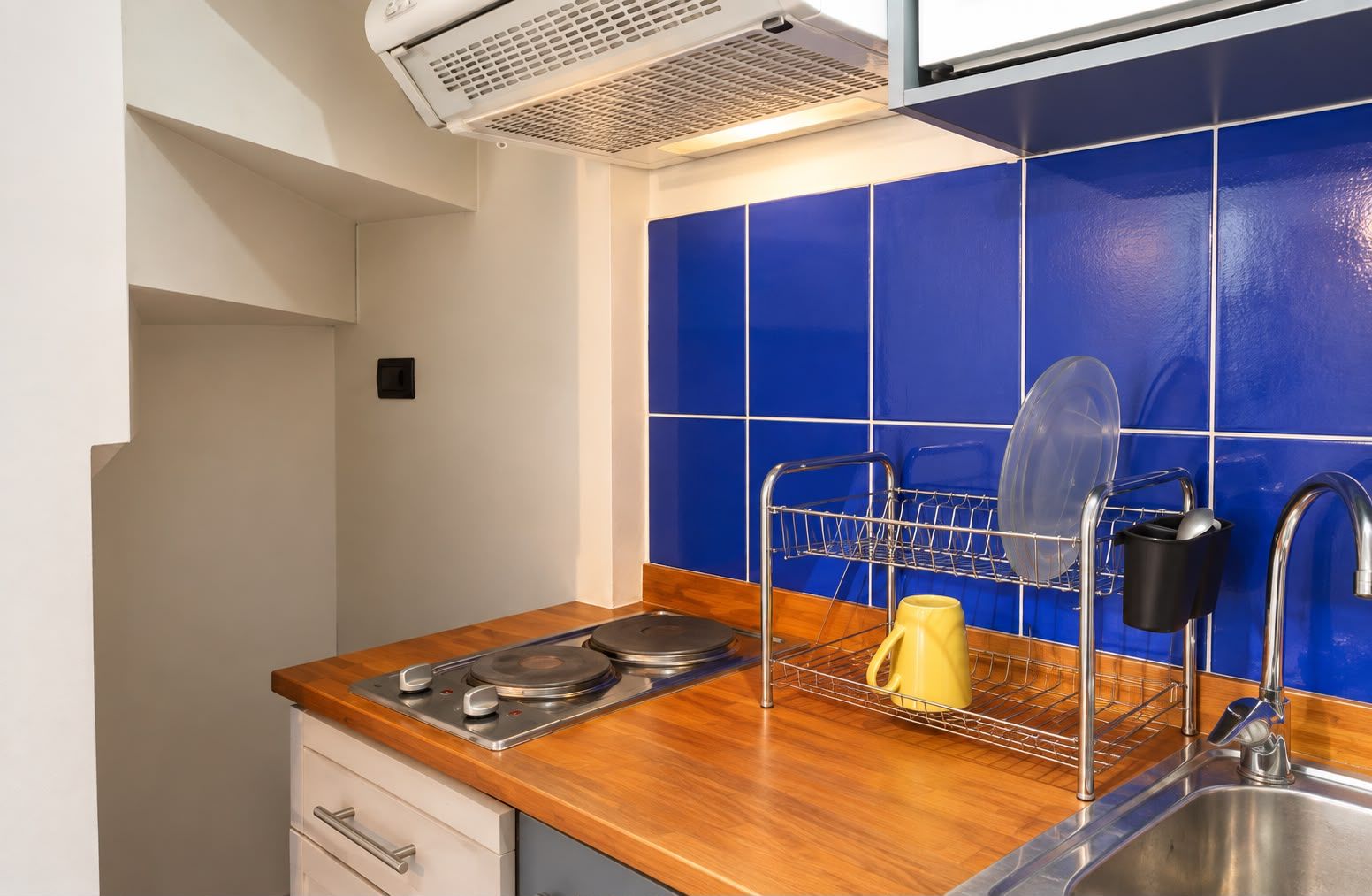A kitchen with a wooden countertop, a dish rack, a yellow mug, and a sink.