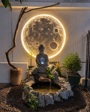 Eine Buddha-Statue in einem Garten, hinter ihr eine leuchtende Installation, die an den Mond erinnert.