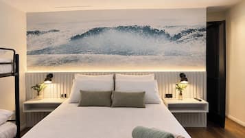 A modern hotel room with a large bed, two bedside tables with lamps, a view of the ocean, and a bunk bed in the corner.