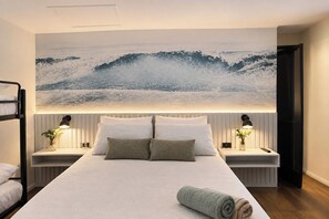 Une chambre d’hôtel moderne avec un grand lit, deux tables de chevet avec des lampes, une vue sur l’océan et un lit superposé dans un coin.