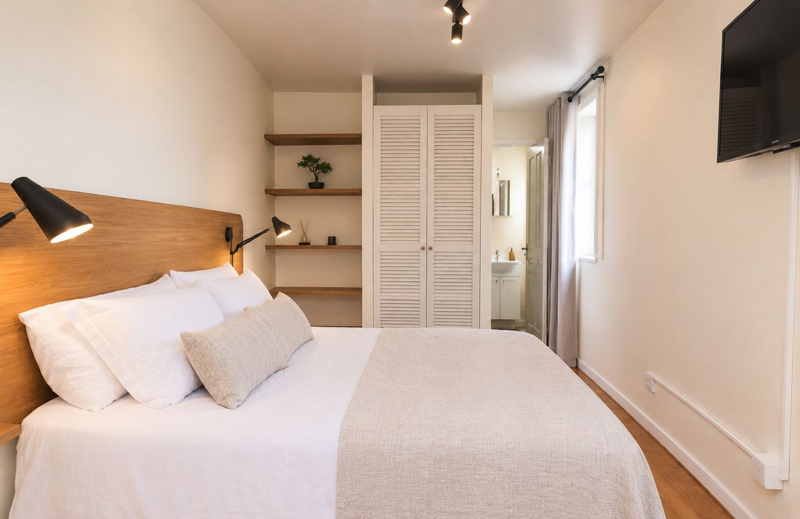 Een slaapkamer met een bed, een bedlampje en een aan de muur bevestigde televisie.