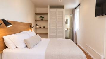 Een slaapkamer met een bed, een bedlampje en een aan de muur bevestigde televisie.