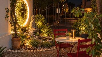 A serene outdoor seating area with a Buddha statue, a round table, and red chairs.
