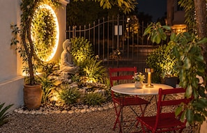 A serene outdoor seating area with a Buddha statue, a round table, and red chairs. - Yogi Hostels (Santiago)