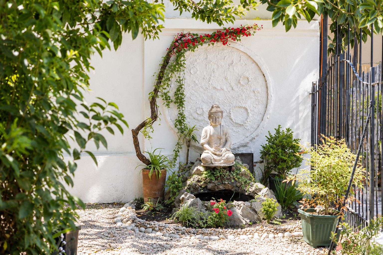 A serene garden with a Buddha statue, a circular wall, and various plants.