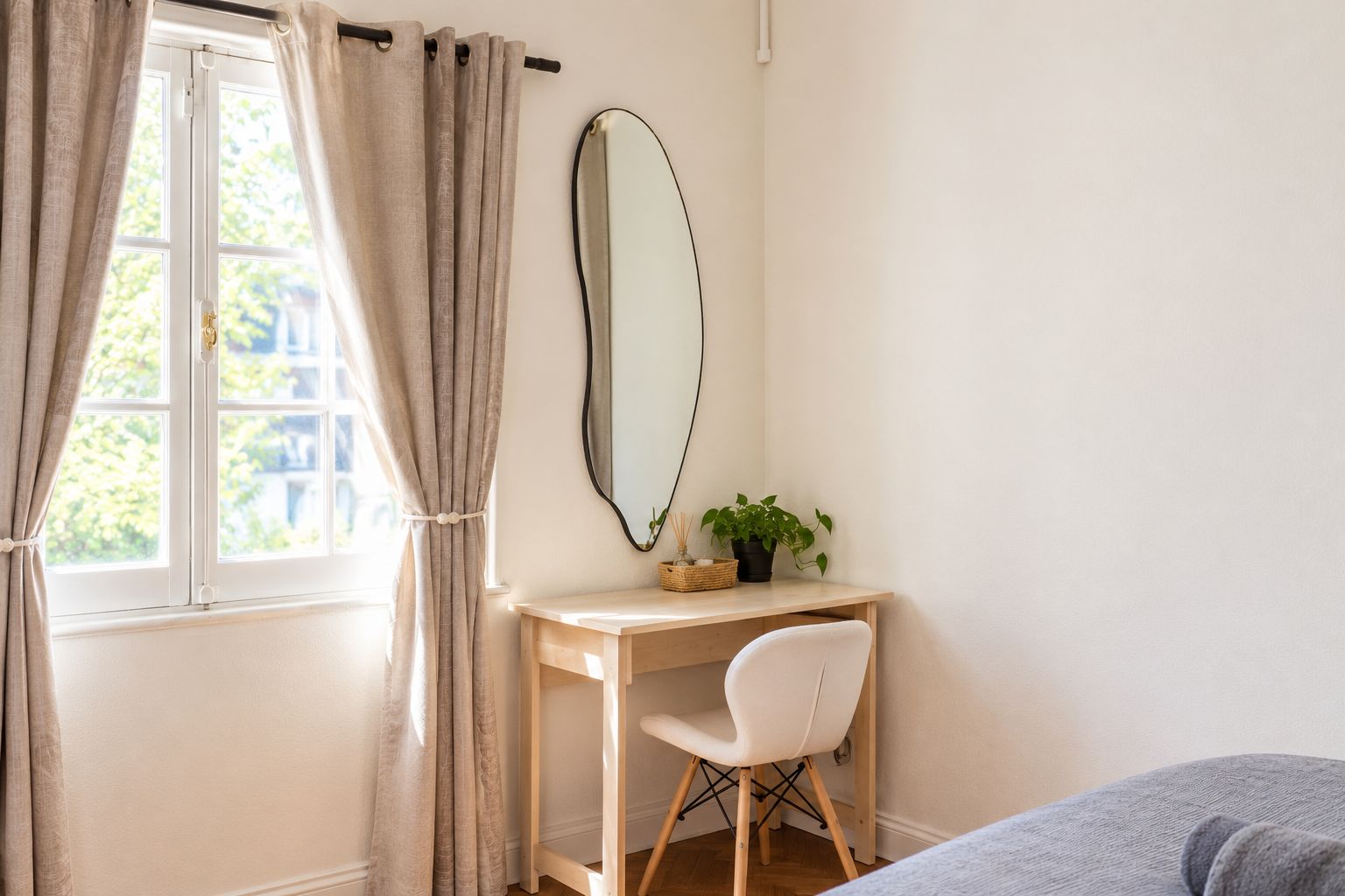 A bedroom with a bed, a desk with a chair, a window with curtains, and a mirror on the wall.