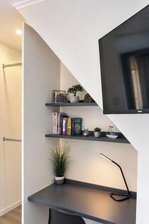 A modern interior with a staircase, a flat-screen TV mounted on the wall, and a shelf with books and decorative items. - Yogi Hostels (Santiago)