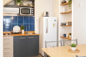 A compact kitchen with a microwave, toaster, and refrigerator, a sink, and a dining area with a table and chairs. - Yogi Hostels (Santiago)