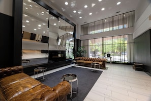 A spacious lobby with a modern design, featuring a leather sofa, a piano, and a large mirror reflecting the room. - 2-Bedroom Condo Townhouse | Fort York & Lake Access (Toronto)
