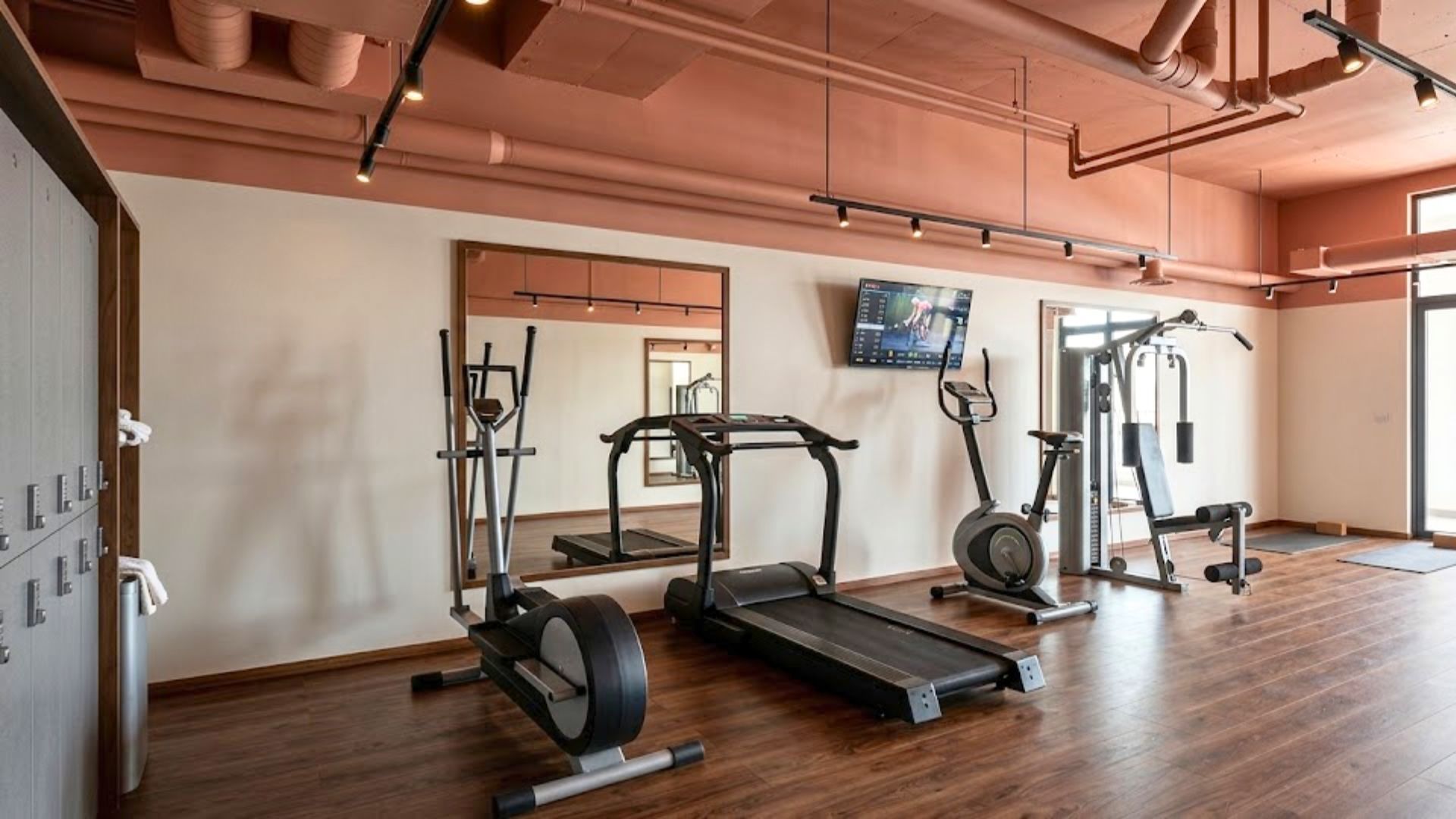 A gym with exercise equipment, a large mirror, and a television on the wall.