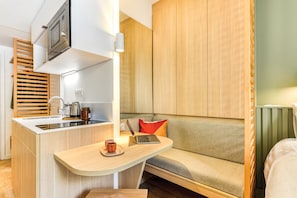 A compact kitchenette with a microwave, sink, and kettle, a wooden cabinet, and a small seating area with a laptop and two cups. - Appart'Hôtel Bikube - Paris Suresnes (Suresnes)