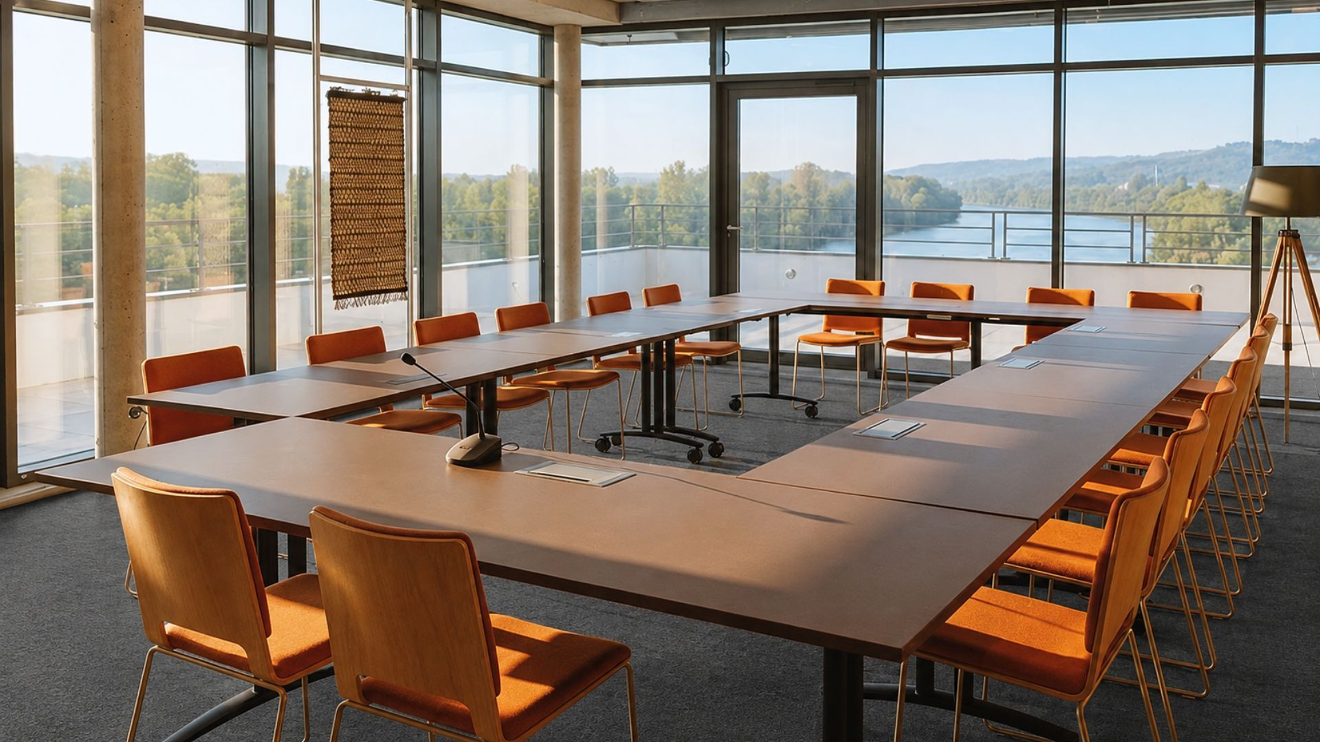 Une salle de conférence avec une longue table et des chaises, de grandes fenêtres donnant sur un lac et des arbres, et une tapisserie murale tissée.