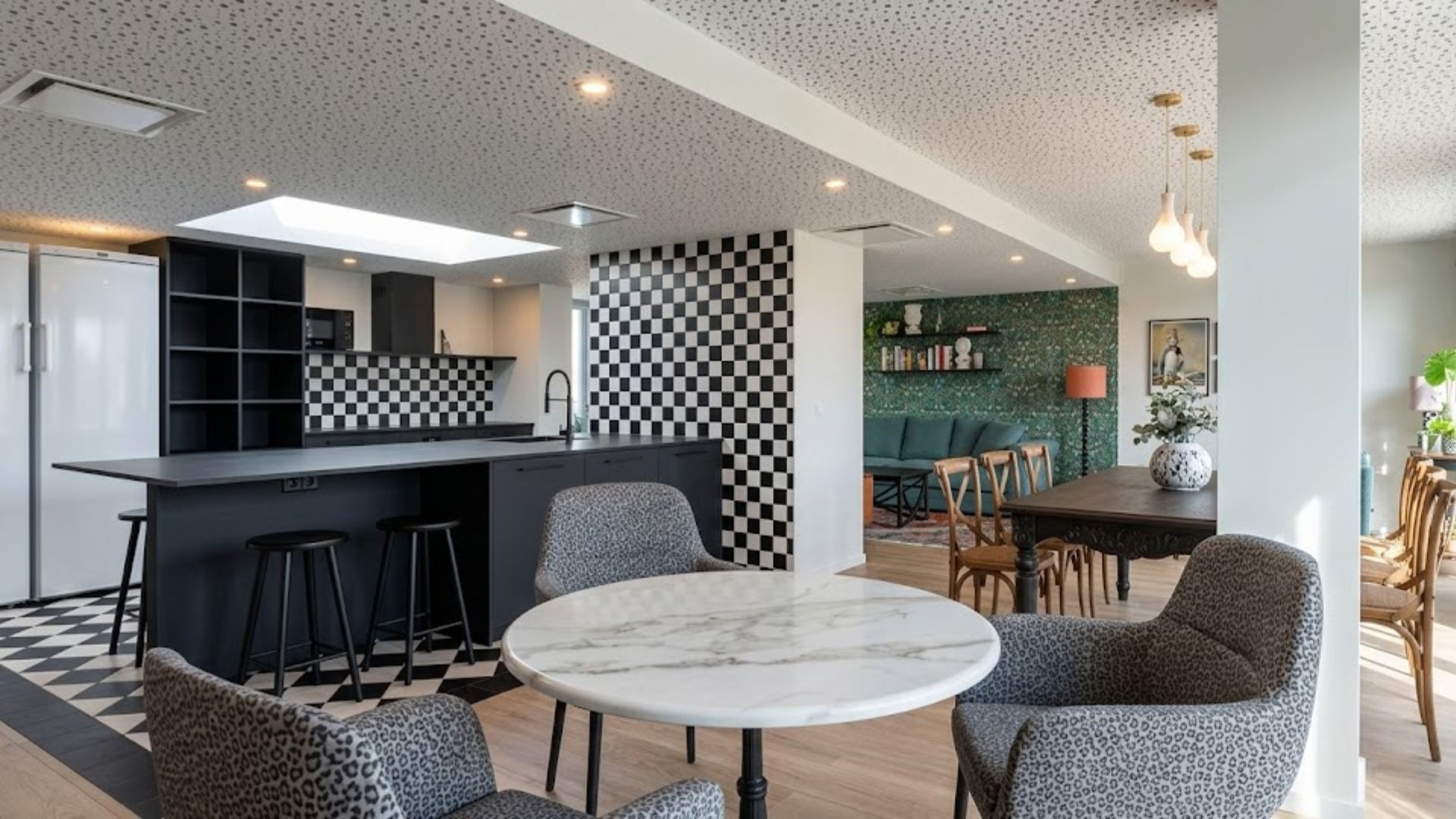 A modern kitchen with a checkered backsplash, a dining area with a round marble table, and a living room with a green sofa.