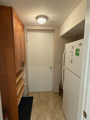 A narrow hallway with a white door at the end, a white refrigerator on the right, and wooden cabinets on the left. - One bedroom basement apartment (Vaughan)