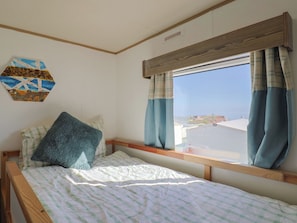 Ein Einzelbett mit einer gestreiften Bettdecke, einem blauen Kopfkissen und einem Fenster mit Vorhängen.