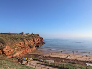 Eine Küstenlandschaft mit einer Klippe, einem Strand und einer kleinen Bebauung auf der Klippe.