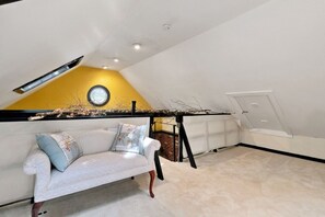 Ein Zimmer mit einem weißen Sofa, einem kleinen Tisch, einem Fenster mit Rundblick und einer schrägen Decke mit eingelassener Beleuchtung.