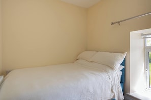 Un llit individual amb roba de llit blanca a una habitació de parets planes i una finestra.