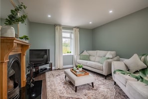 A living room with a fireplace, television, sofa, and a window with curtains. - Newly Renovated Farmhouse (KY)
