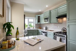 A kitchen with light green cabinets, a white countertop, a stove, and a window with a view of greenery. - Newly Renovated Farmhouse (KY)