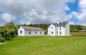 A two-story white house with a grey roof, surrounded by a well-maintained lawn and dense trees. - Newly Renovated Farmhouse (KY)