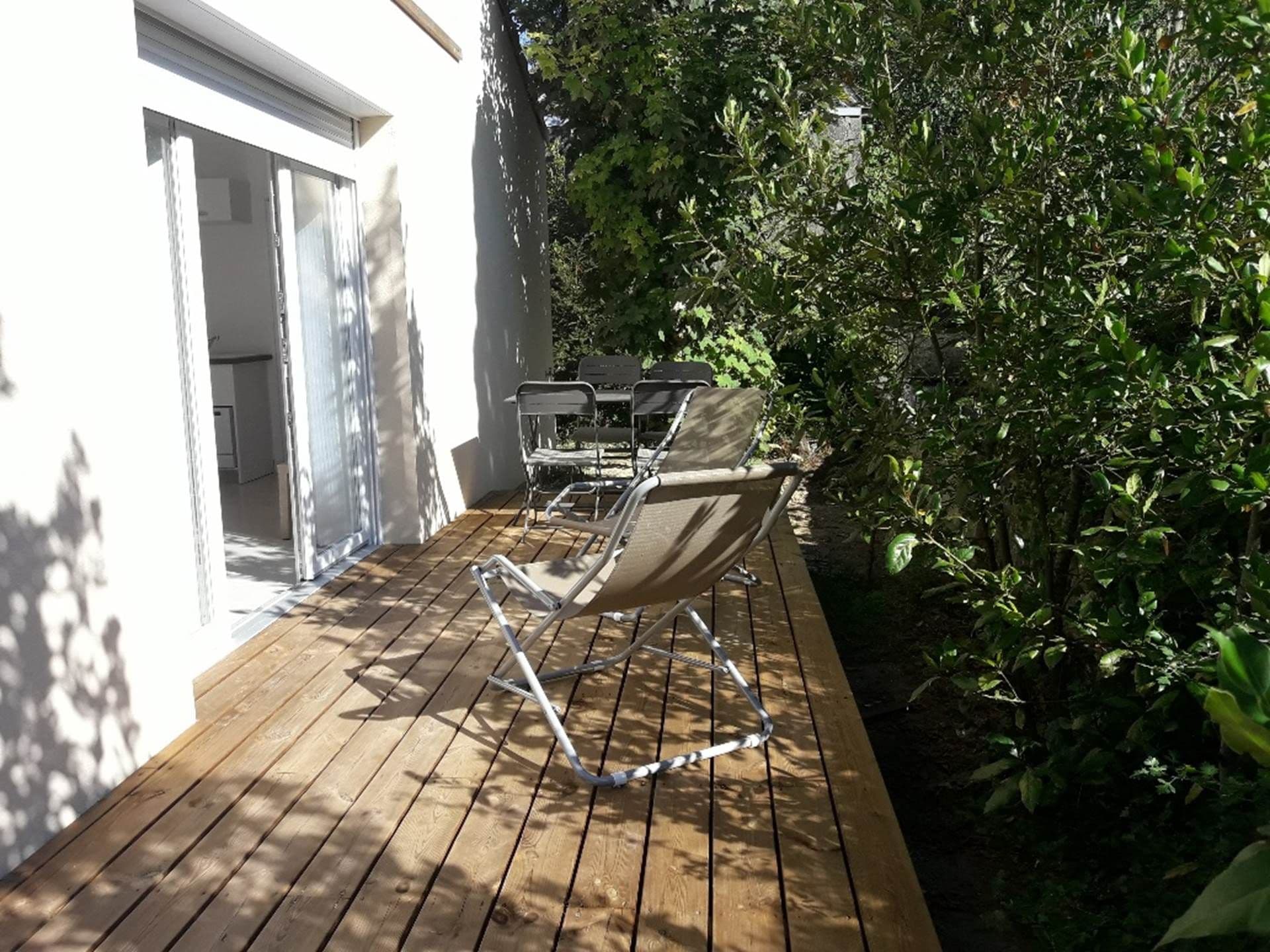 A wooden deck with a chair and a table, surrounded by greenery.