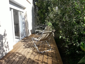 A wooden deck with a chair and a table, surrounded by greenery. - 4-Star Furnished Studio (West-Facing) (JONZAC)