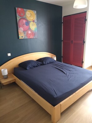 Ein Schlafzimmer mit einem Bett, einem Nachttisch, einer Lampe, einem Wandbild und einer roten Tür.