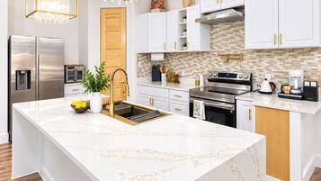 A modern kitchen with white cabinetry, a marble island, stainless steel appliances, and a chandelier.