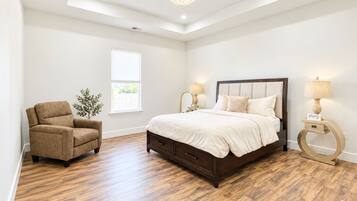 A bedroom with a large bed, a chair, a bedside table, a lamp, and a window.