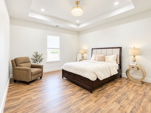 A bedroom with a large bed, a chair, a bedside table, a lamp, and a window.