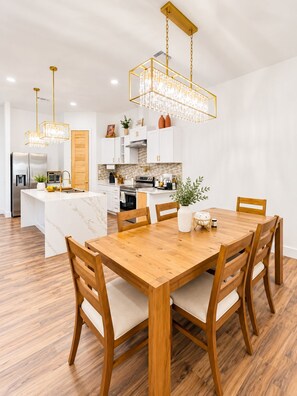 A modern kitchen with white cabinetry, a marble island, and a wooden dining table with chairs.