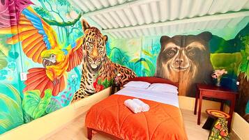 A room with a bed, a mural of a tiger and a parrot, and a small table with a vase.