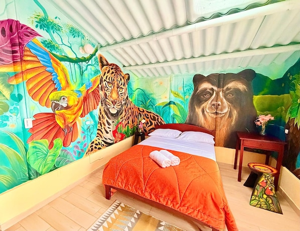 A room with a bed, a mural of a tiger and a parrot, and a small table with a vase.