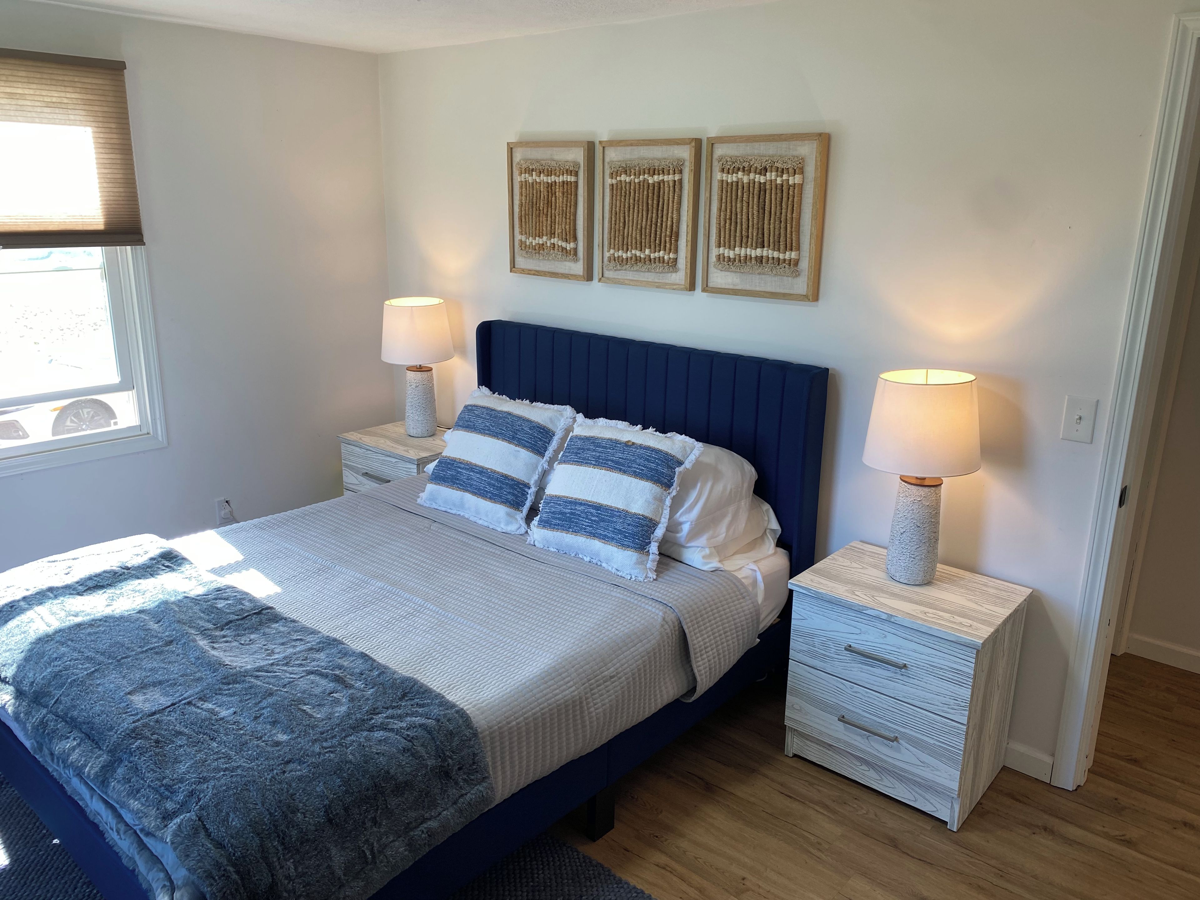 Une chambre à coucher avec un lit, deux tables de chevet, une fenêtre et des œuvres d’art murales.