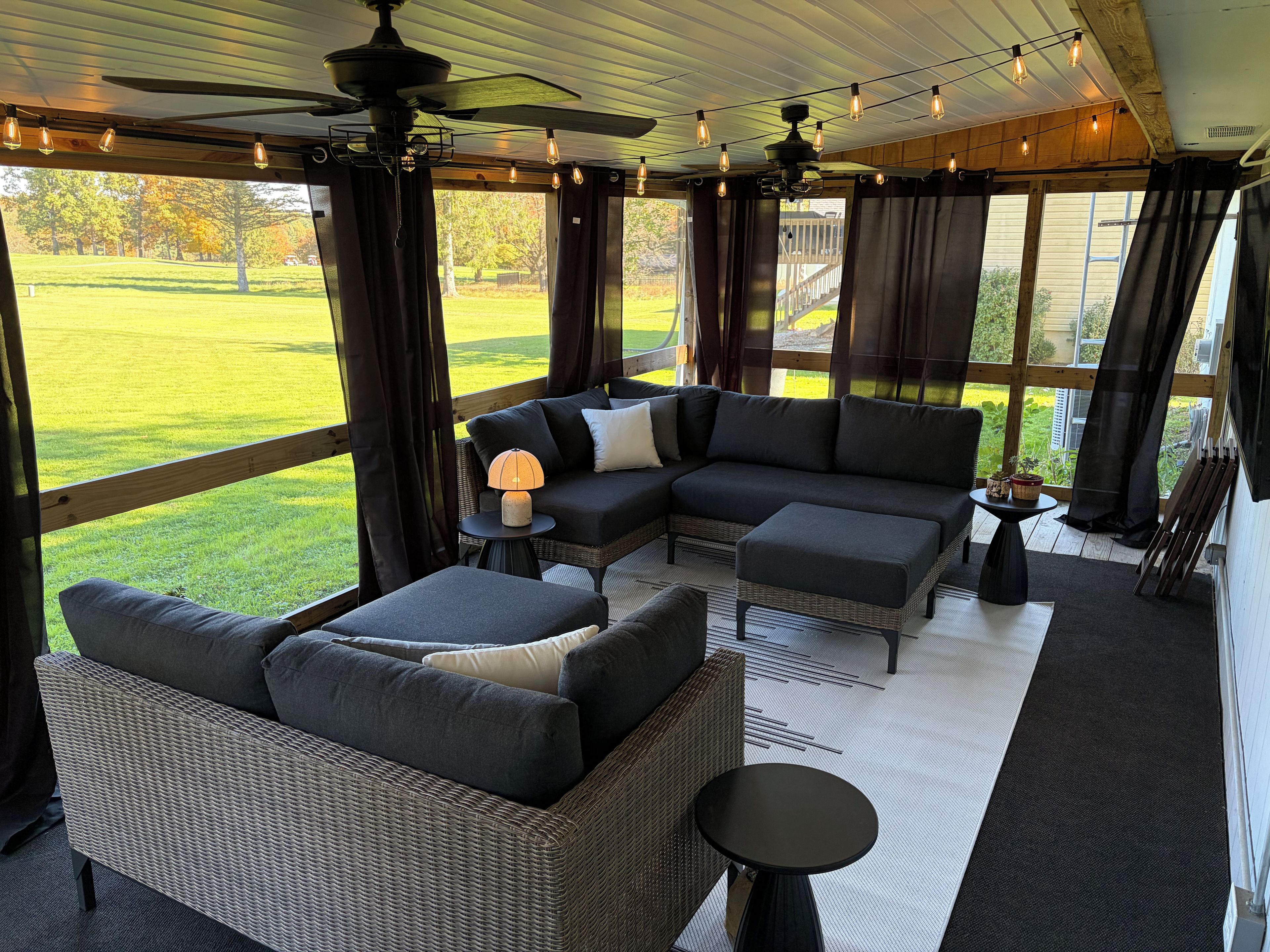 Un'area salotto esterna coperta, con un divano componibile, un tavolino e una ventola a soffitto.