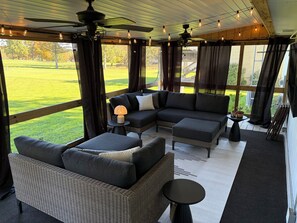 A covered outdoor seating area with a sectional sofa, a small table, and a ceiling fan.