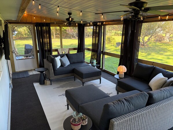 A spacious room with a large window, a ceiling fan, and a sofa set.