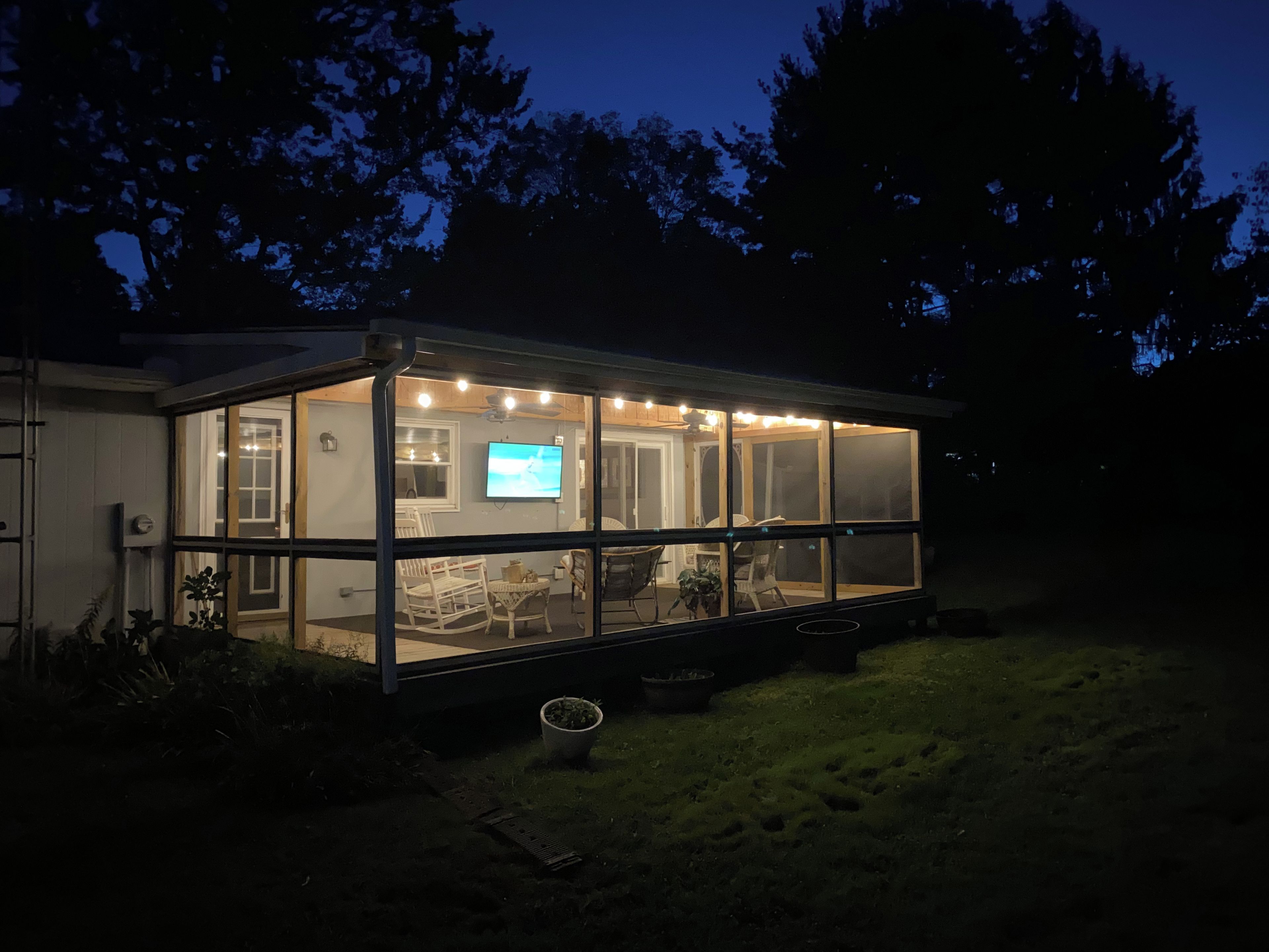A house with a large glass enclosure, a television, and outdoor seating.