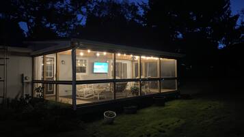 A house with a large glass enclosure, a television, and outdoor seating.