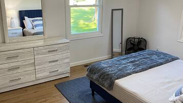 Une chambre à coucher avec un lit, une commode, un miroir, une fenêtre et un ventilateur.
