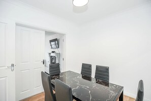 Comedor con mesa de mármol negro y cuatro sillas, una puerta blanca y una chimenea con un televisor encima.