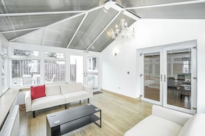 A spacious living room with a high ceiling, a chandelier, a sofa set, and a sliding glass door leading to a kitchen area. - Hot Tub,Parking,Nr Edinburgh,Contractor Stay,4BED (East Lothian)